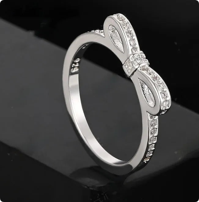 Silver couple style ring with a rhinestone and zircon crystal bow design on a finger.