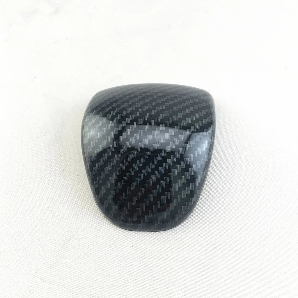 Black gear shift cover with a carbon fibre pattern for car interior styling.