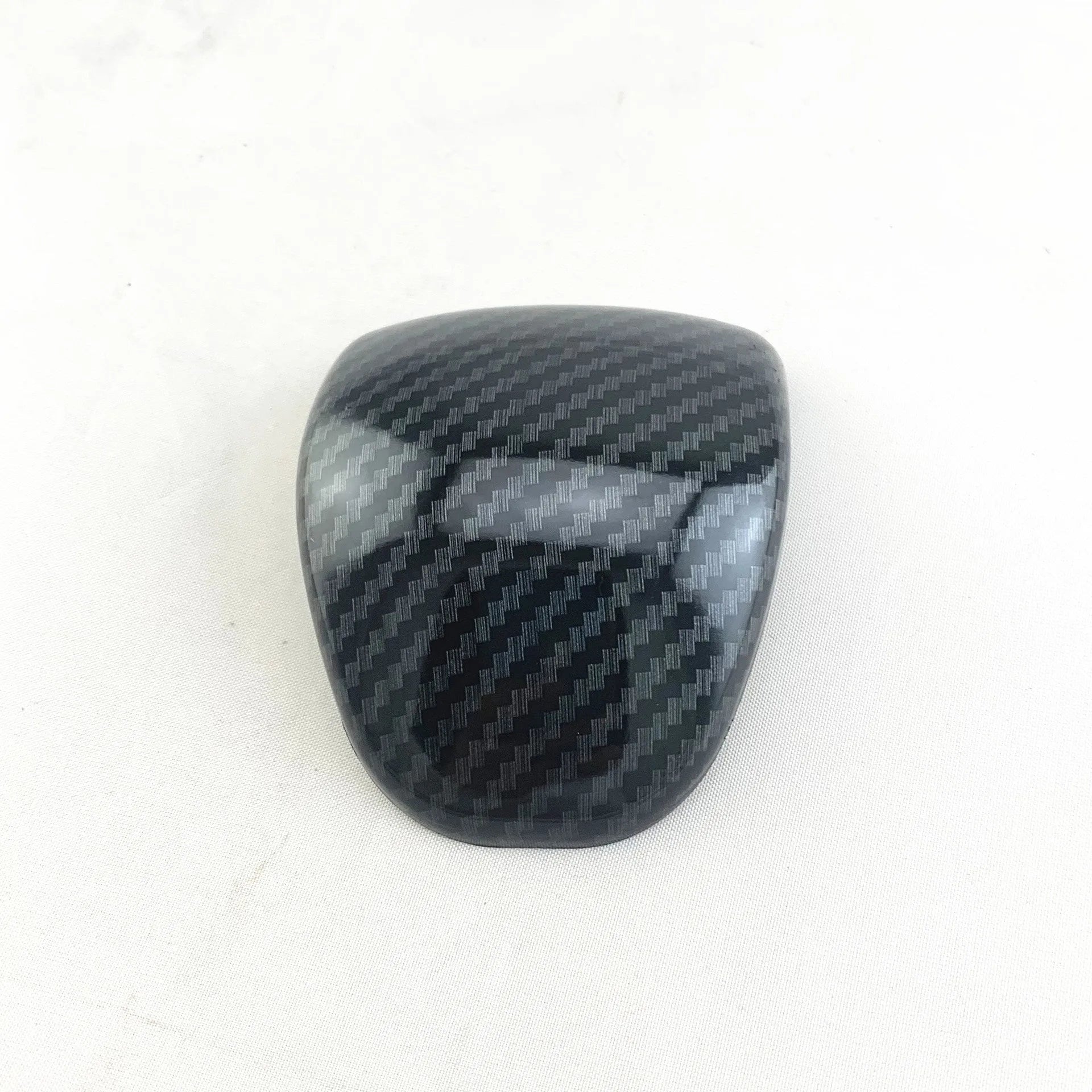 Black gear shift cover with a carbon fibre pattern for car interior styling.
