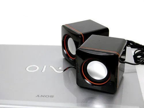 Black square USB computer speaker on desktop next to monitor