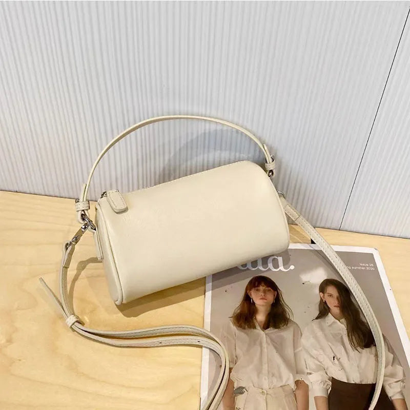 Soft genuine leather cylindrical crossbody bag for mobile phones, shown in a street style with visible stitching.