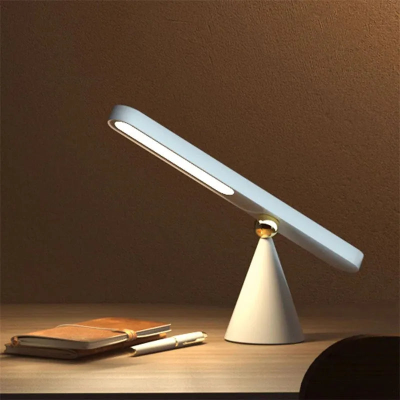 White geometric USB desk lamp with magnetic base shown on a wooden desk.
