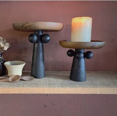 Round natural wooden tray with high legs holding a candle and perfume bottle on a table.