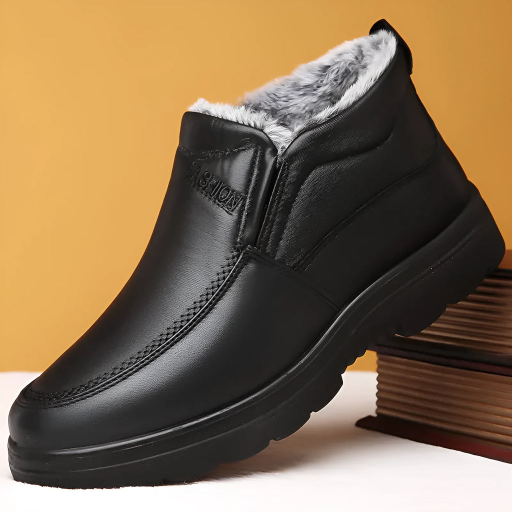 Men's black and brown fleece-lined winter slip-on shoes with rubber soles on a wooden floor.