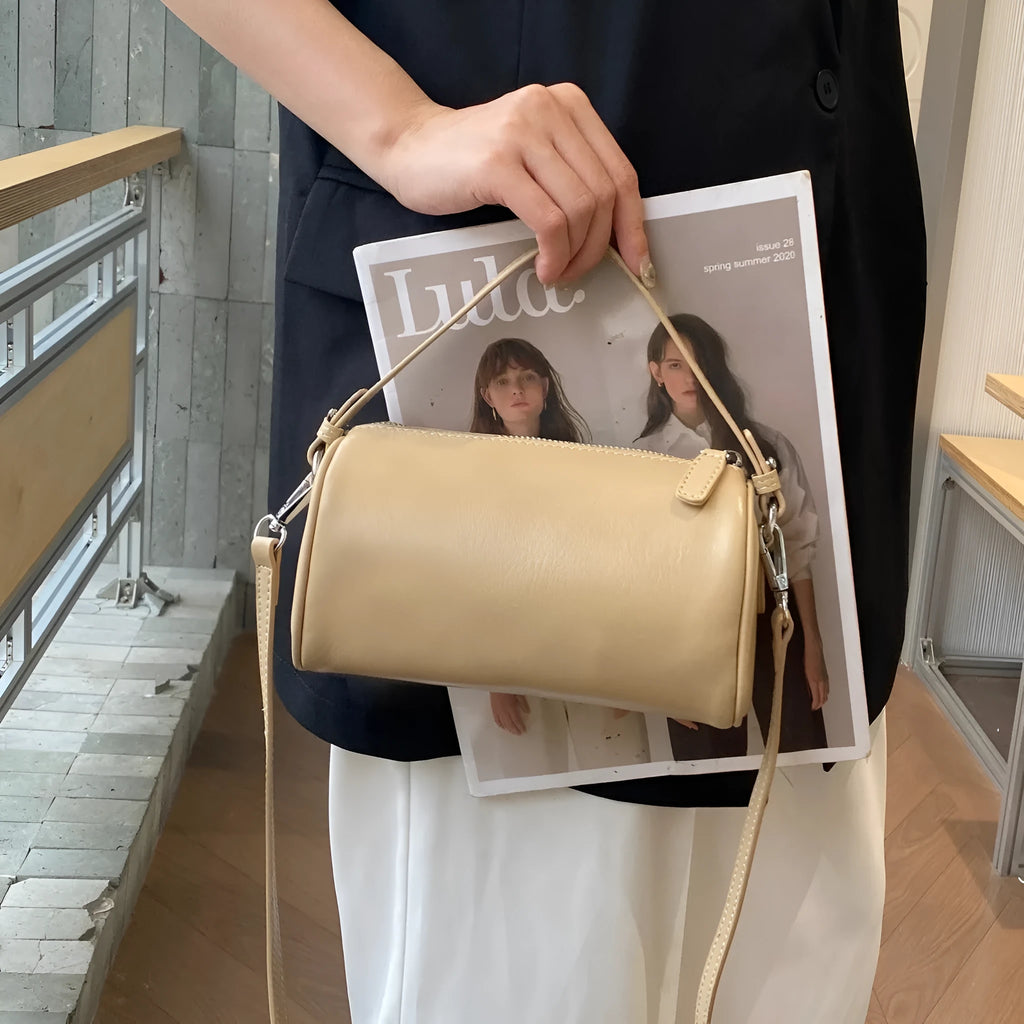 Soft genuine leather cylindrical crossbody bag for mobile phones, shown in a street style with visible stitching.