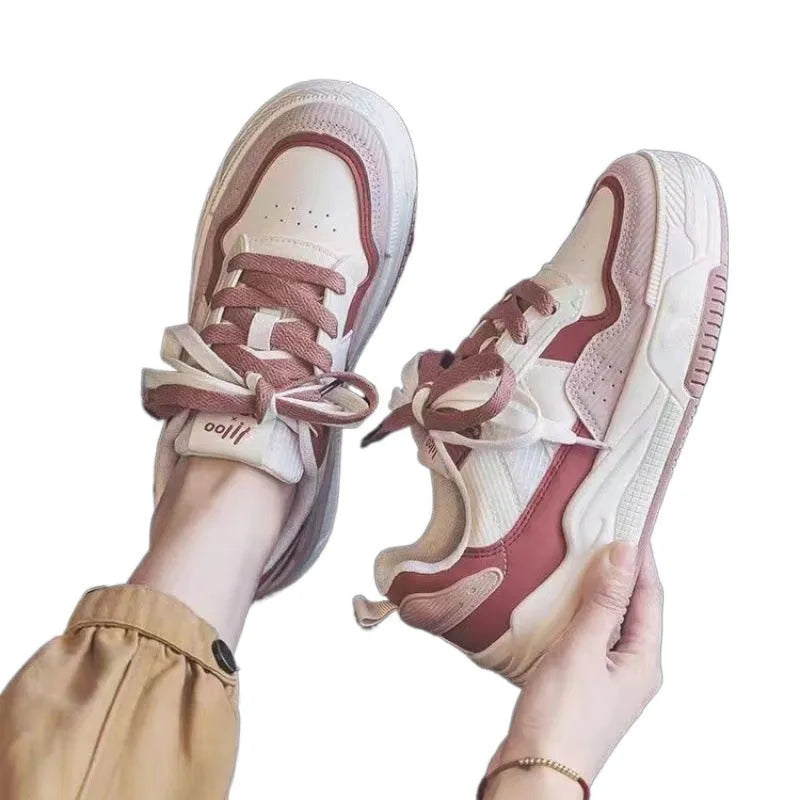 Pink and beige low top women's sneakers with a rubber sole on a neutral background.