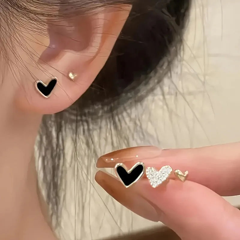 Set of three pairs of women's heart-shaped stud earrings in gold, black, white, and pink.