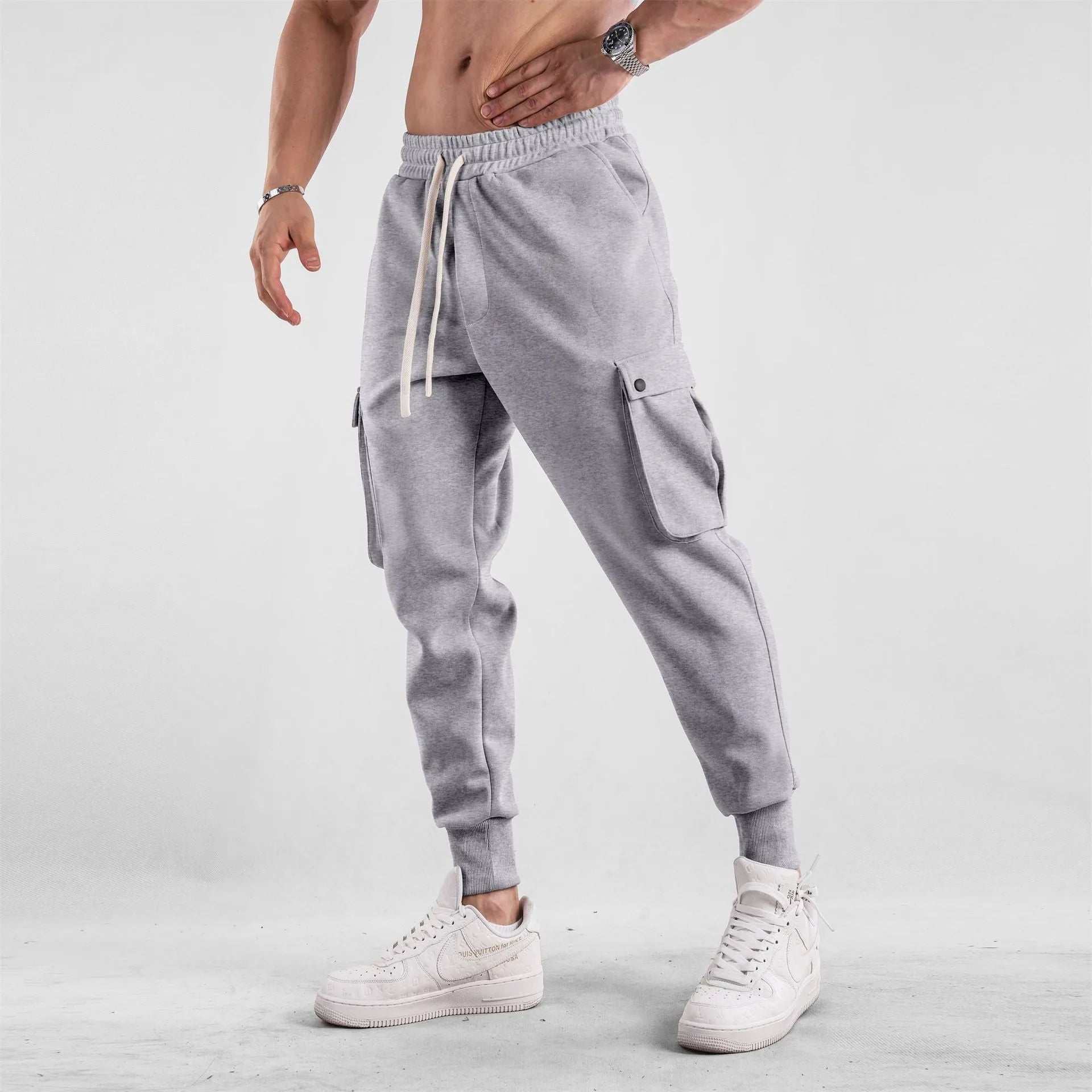 Man wearing loose light grey cotton trousers with ankle tie and multiple pockets, style of American sports leisure wear.