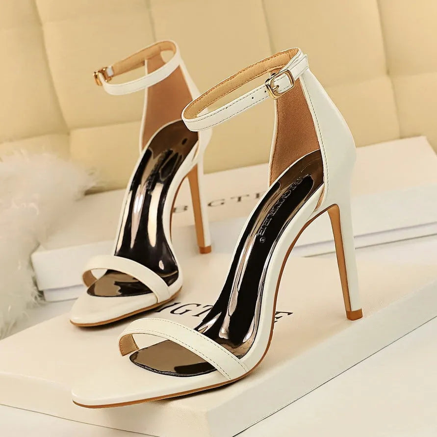 White high-heeled sandal with an open toe and a buckle-fastened ankle strap.