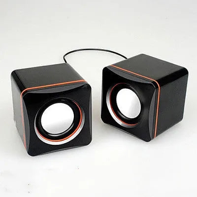 Black square USB computer speaker on desktop next to monitor
