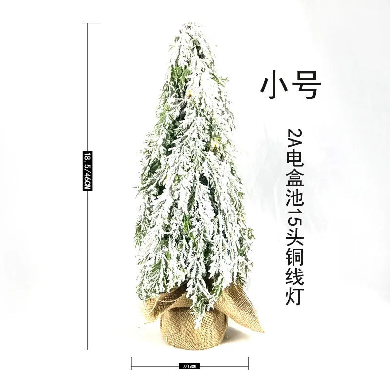 Small white artificial Christmas tree with snowy textured branches and built-in lights on a desktop