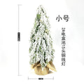 Small white artificial Christmas tree with snowy textured branches and built-in lights on a desktop