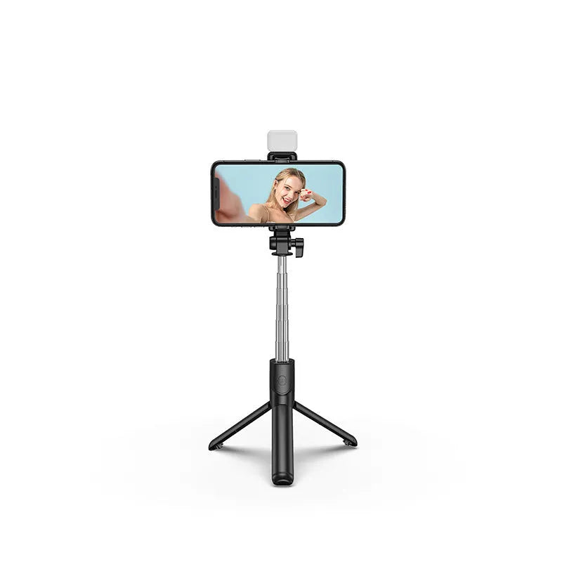 Black Bluetooth selfie stick tripod with phone holder, fill light, and remote control on a table.
