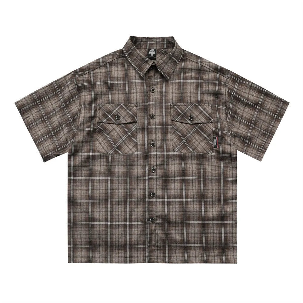 Man wearing a black and brown plaid short sleeve shirt with embroidered letters on the lapel