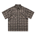 Man wearing a black and brown plaid short sleeve shirt with embroidered letters on the lapel