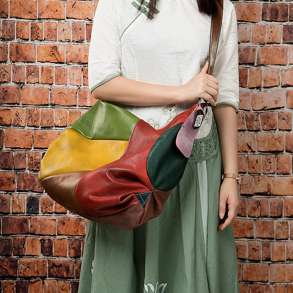 Brown cowhide leather crossbody travel bag with stitching detail, shown with a laptop and magazine.