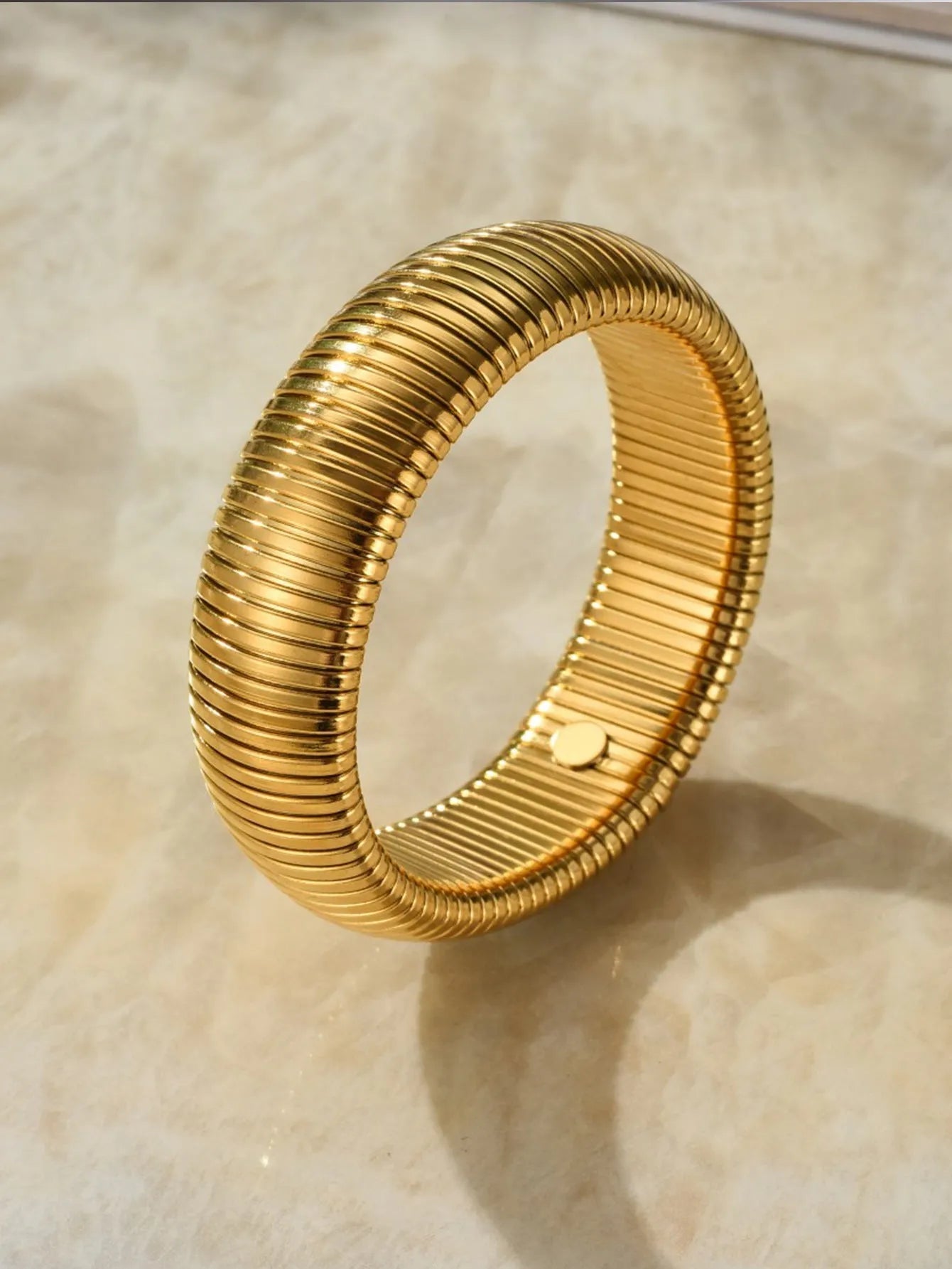 Close-up of a women's elastic titanium steel bracelet featuring a bold vertical stripe ring pattern in a gold tone finish.