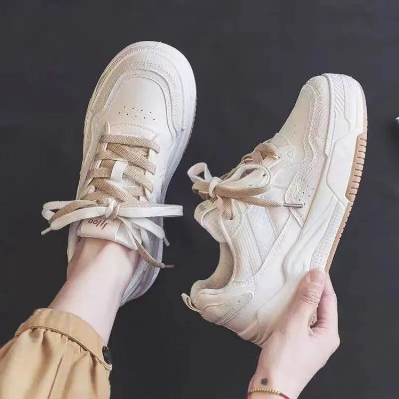 Pink and beige low top women's sneakers with a rubber sole on a neutral background.