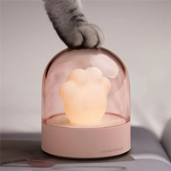 Grey or pink cat paw shaped USB rechargeable night light with music box function on a desk.