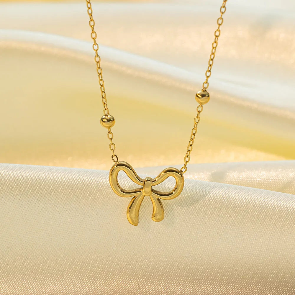 Gold electroplated bow necklace with adjustable chain on dark background