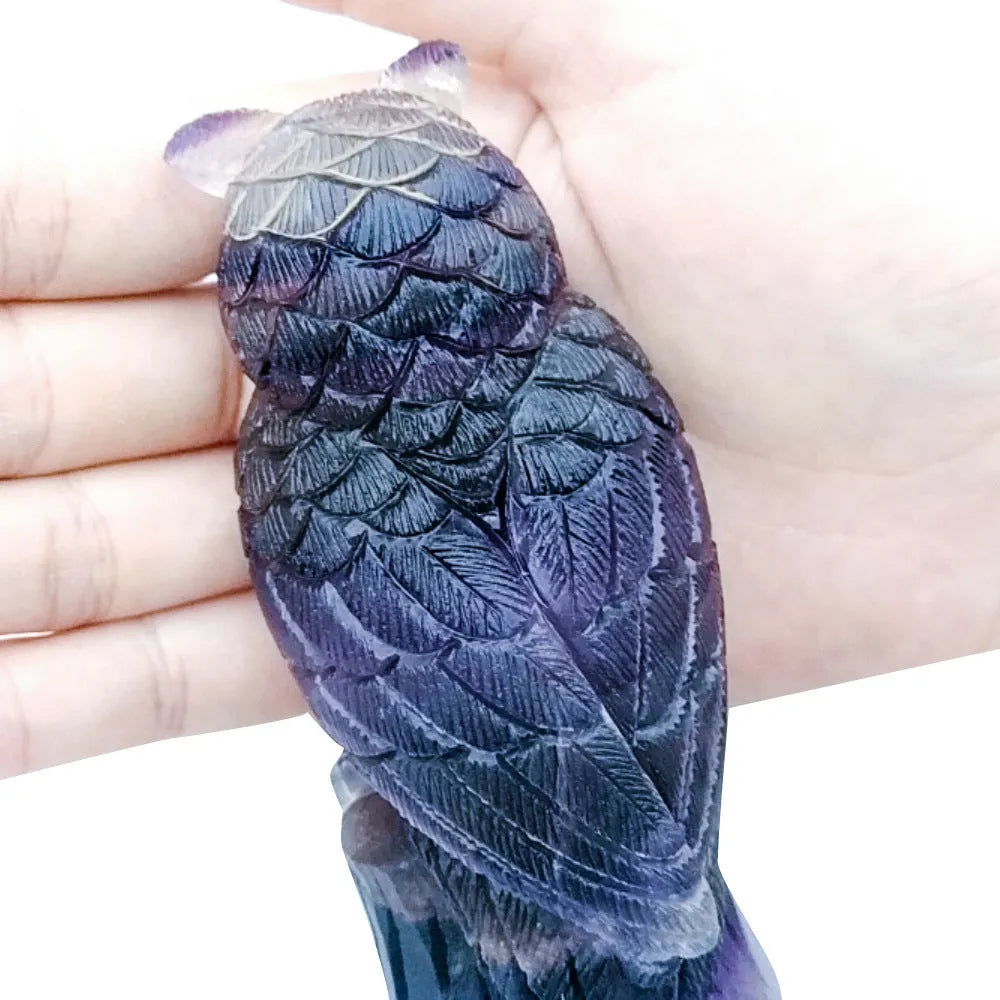 Hand carved purple fluorite stone owl ornament on a wooden surface.