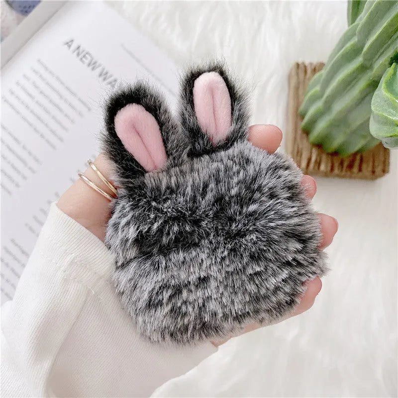 Plush pink silicone AirPods protective cover with cute raised rabbit ears on a white charging case.