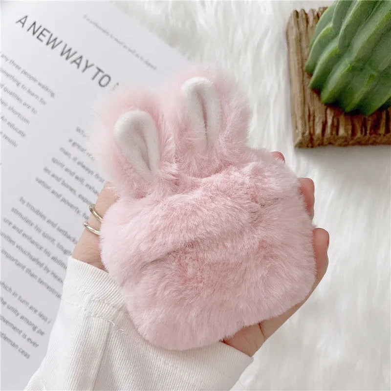 Plush pink silicone AirPods protective cover with cute raised rabbit ears on a white charging case.