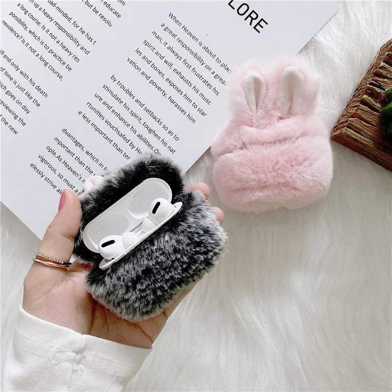 Plush pink silicone AirPods protective cover with cute raised rabbit ears on a white charging case.