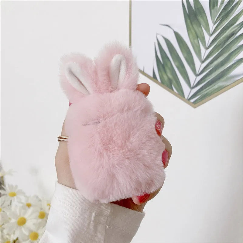 Plush pink silicone AirPods protective cover with cute raised rabbit ears on a white charging case.