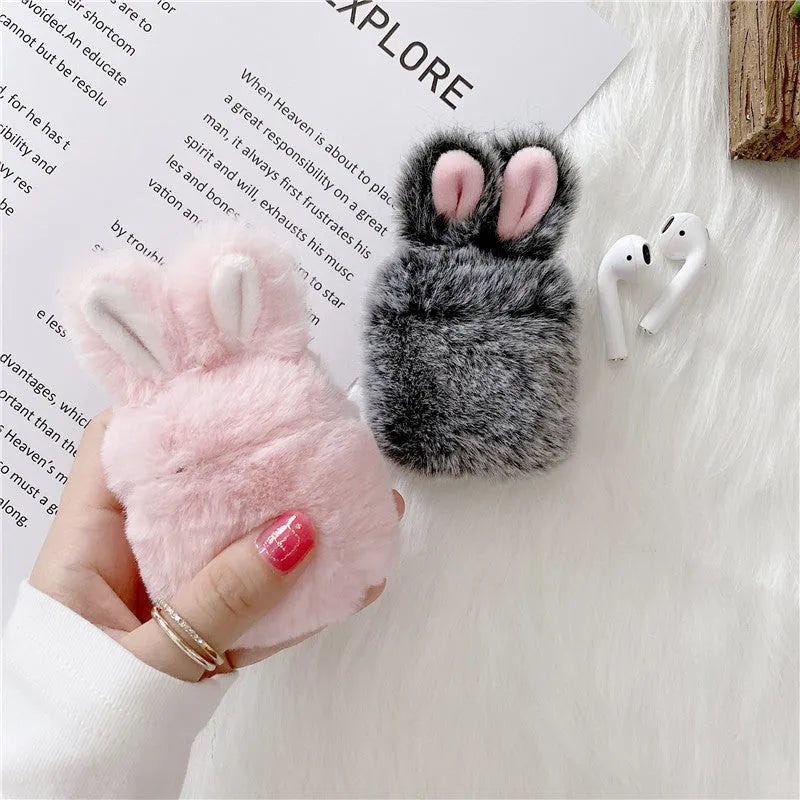 Plush pink silicone AirPods protective cover with cute raised rabbit ears on a white charging case.