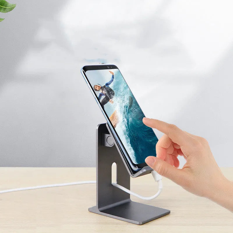 Dark grey alloy lazy bracket phone holder clamped to a desk edge, holding a mobile phone.