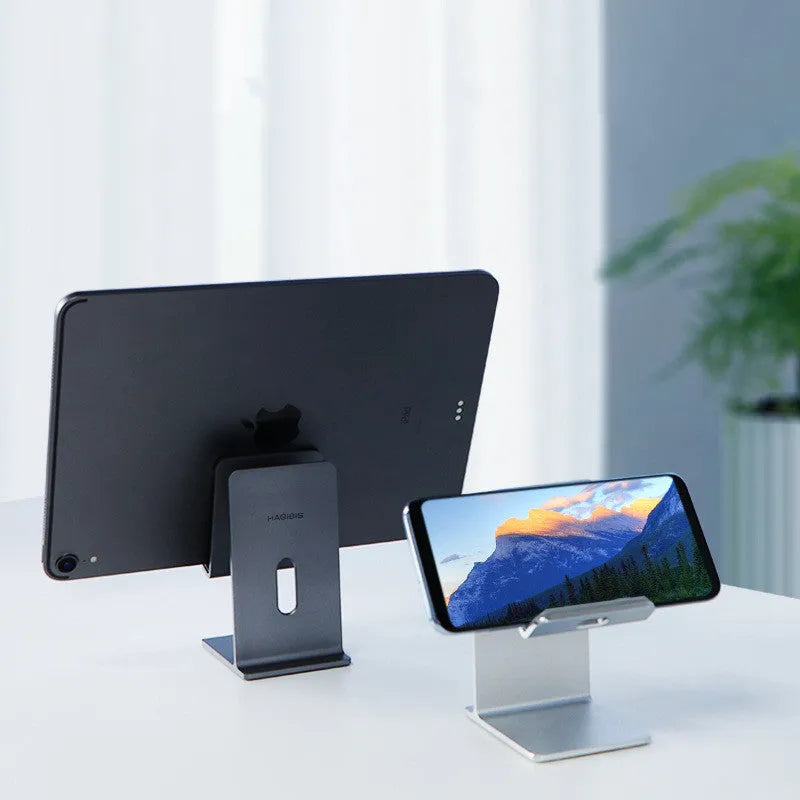 Dark grey alloy lazy bracket phone holder clamped to a desk edge, holding a mobile phone.