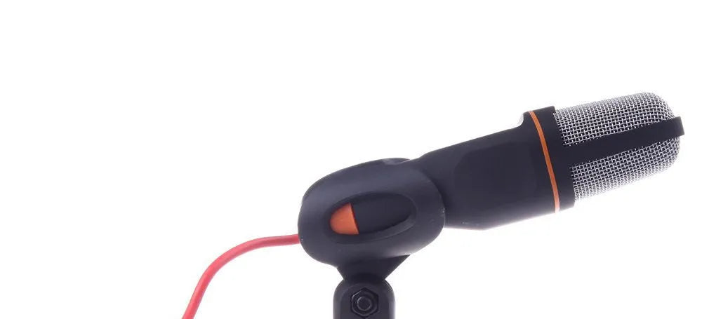 Black wired PC microphone with a metal clip holder on a desk next to a computer.