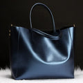 Women's black cowhide leather shoulder bag with a shoulder strap, shown next to a bronze coloured version.