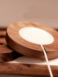 Solid walnut wood magnetic wireless charging bracket base for Magsafe iPhones on a desktop.