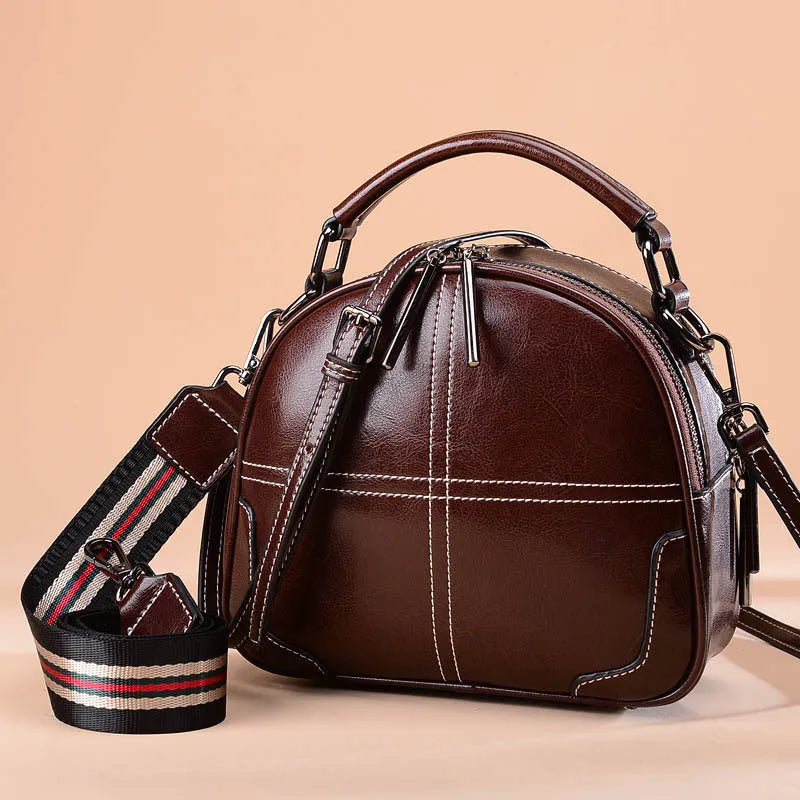 Round leather handbag with dual soft handles in wine red colour, showing zipper closure and compact shape.