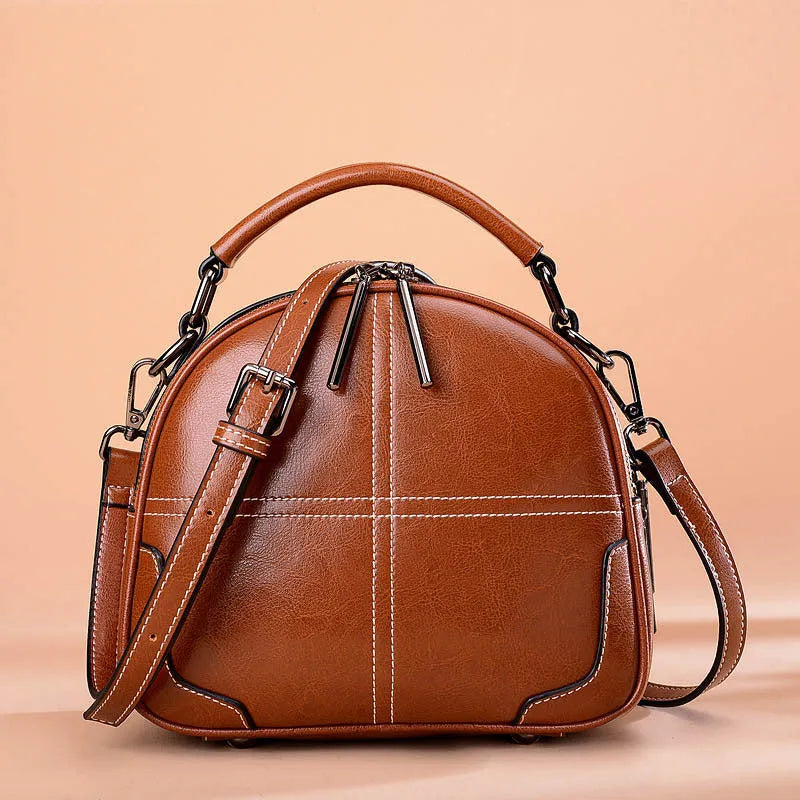 Round leather handbag with dual soft handles in wine red colour, showing zipper closure and compact shape.
