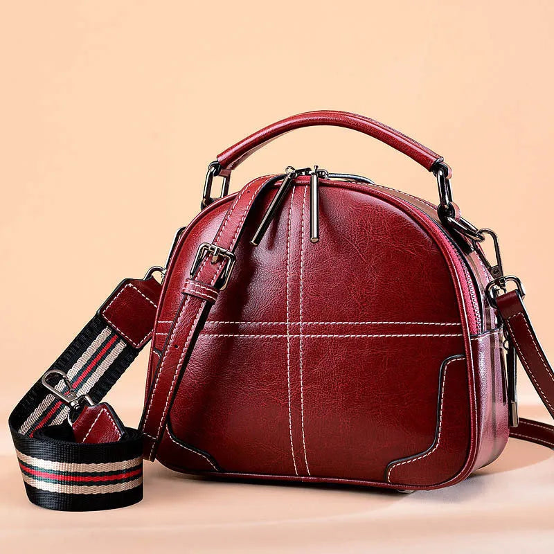 Round leather handbag with dual soft handles in wine red colour, showing zipper closure and compact shape.
