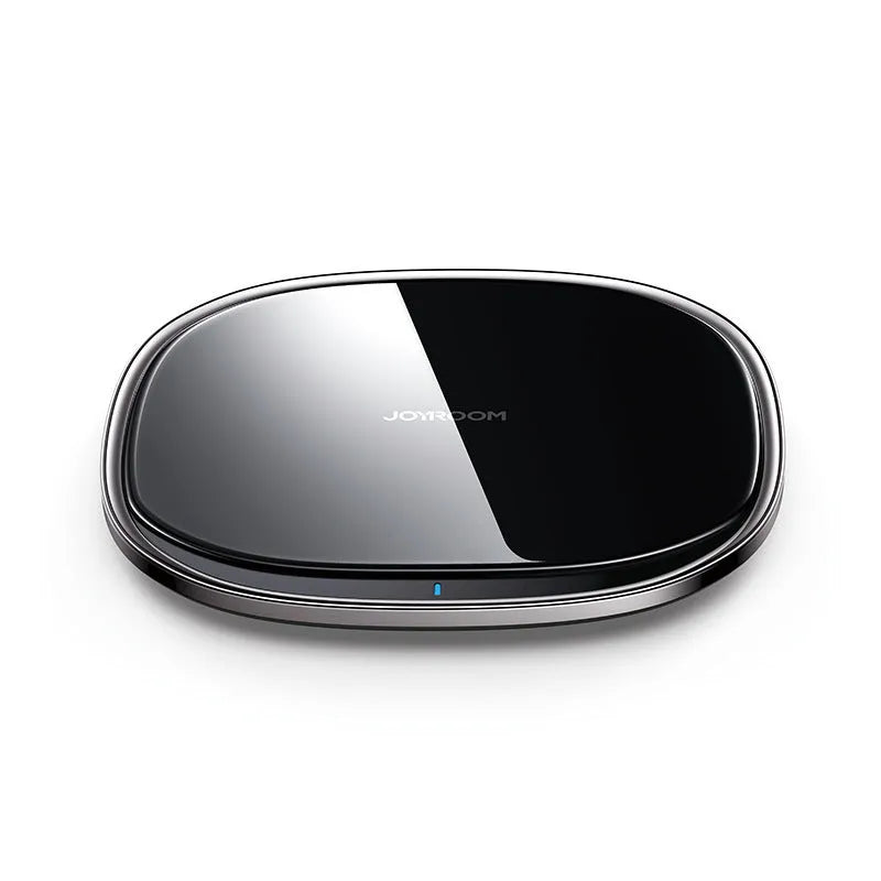 Black 15W wireless phone charger on a wooden desk next to a mobile phone.