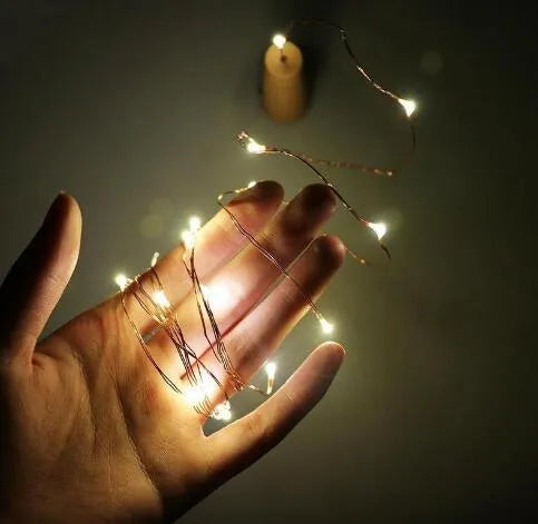 Silver copper wire LED string lights wrapped around a wine bottle with bottle stopper