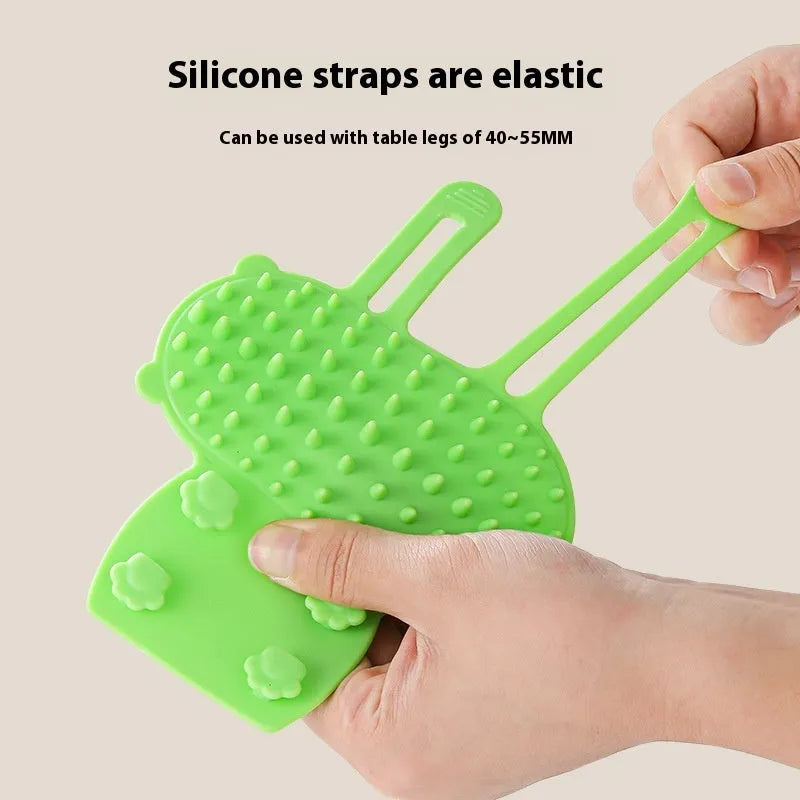 Silicone cat grooming comb with adjustable strap mounted on a table leg, shown in assorted colours.