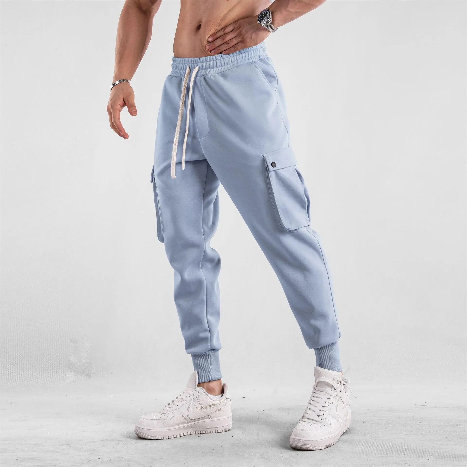 Man wearing loose light grey cotton trousers with ankle tie and multiple pockets, style of American sports leisure wear.