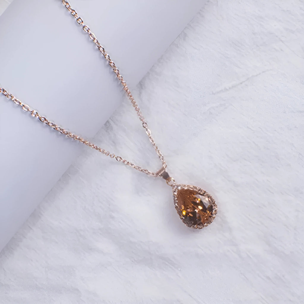 Pink water drop shaped rhinestone necklace with rose gold electroplated alloy pendant on white background