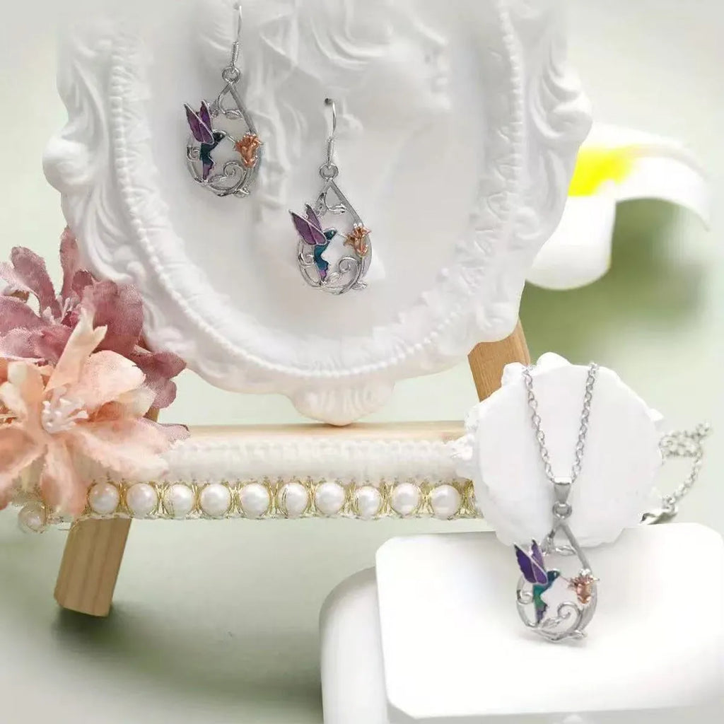 White electroplated copper hummingbird necklace and earring set with animal motifs on a neutral background