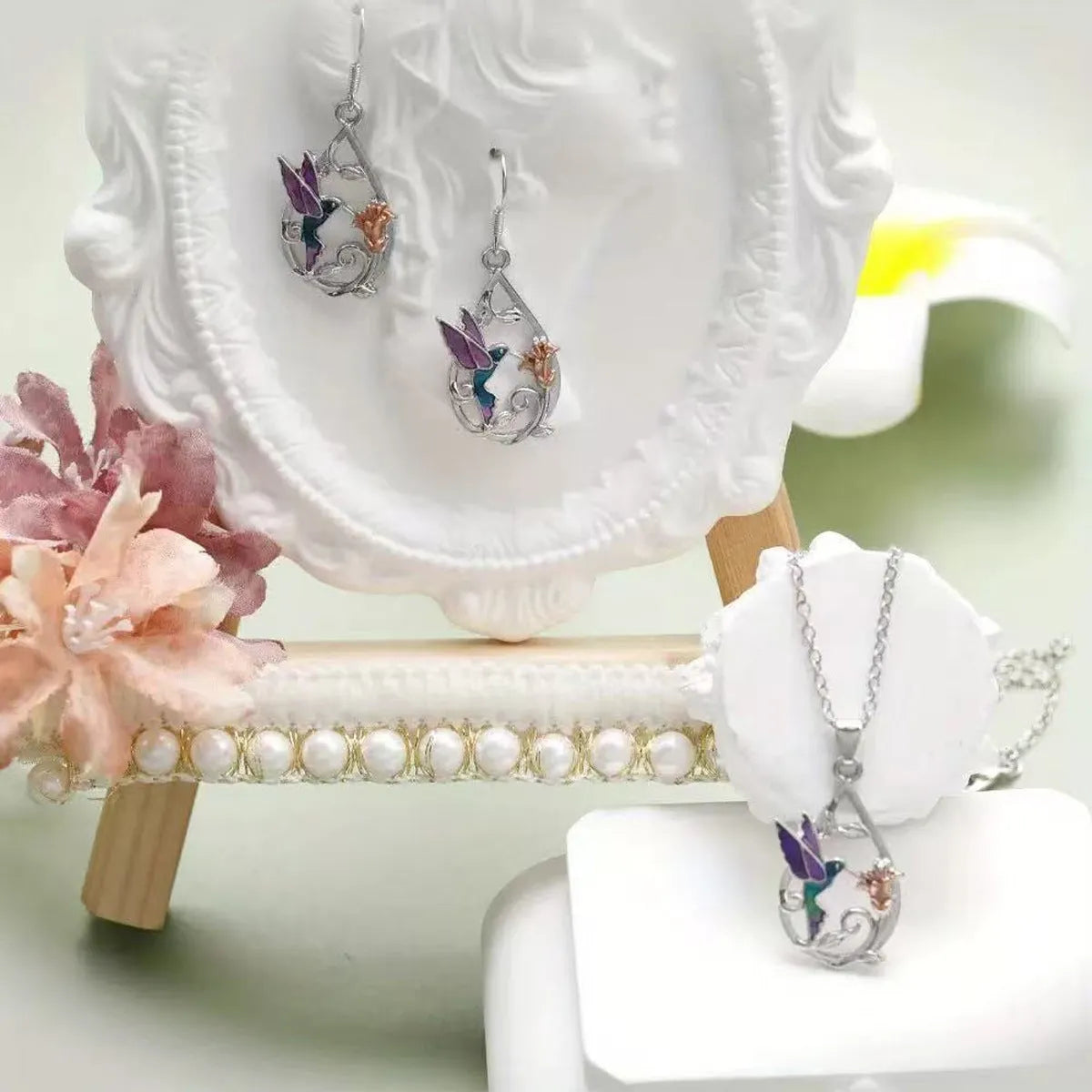 White electroplated copper hummingbird necklace and earring set with animal motifs on a neutral background