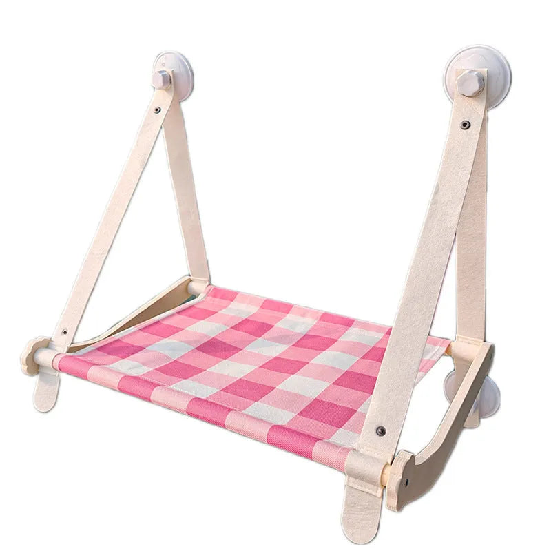 Pink wooden cat hammock with suction cups attached to a window, showing a cat resting on the linen fabric.
