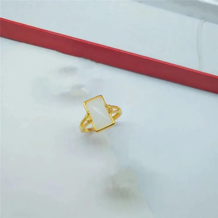 Adjustable brass gold-plated ring with a central green artificial gemstone on a finger.