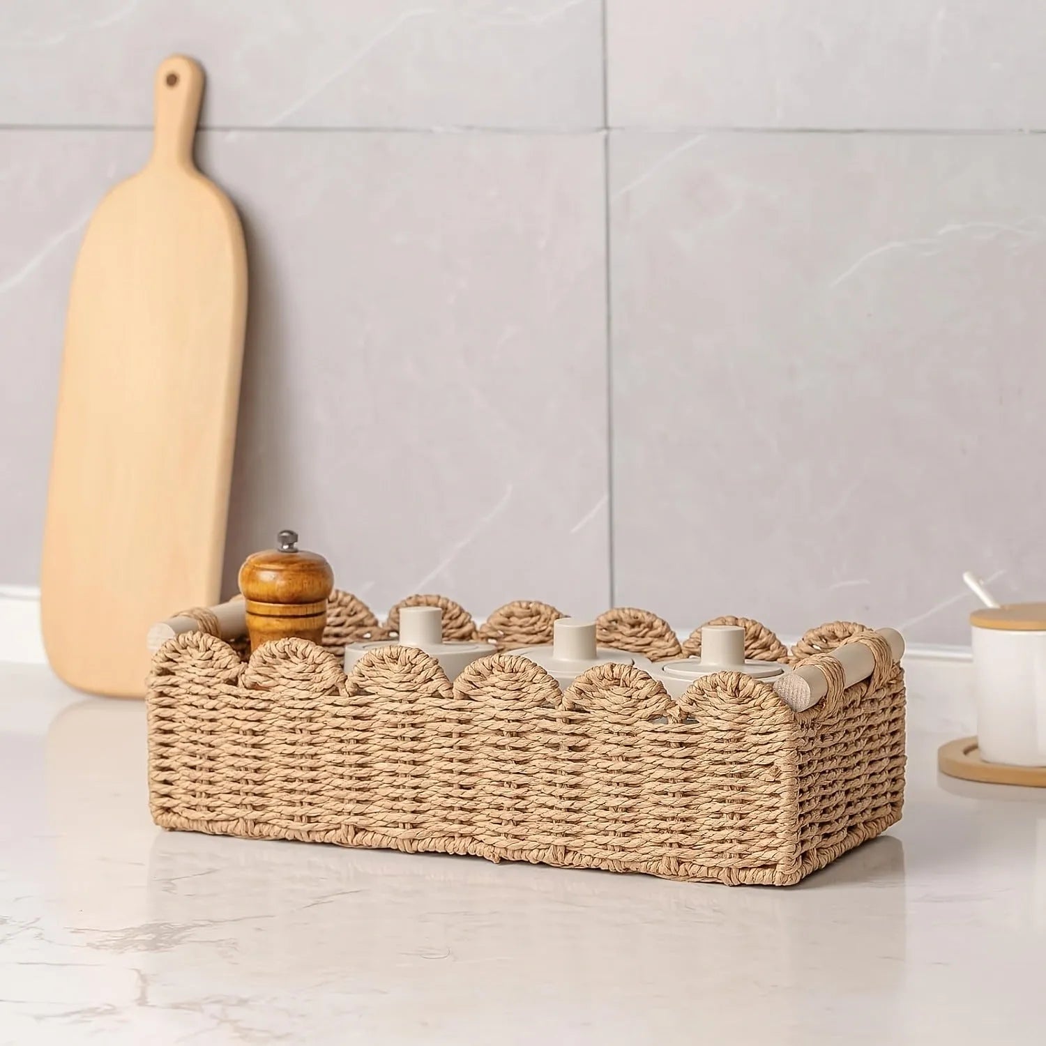 Woven paper storage basket in khaki colour on a desktop, holding remote controls and stationery.