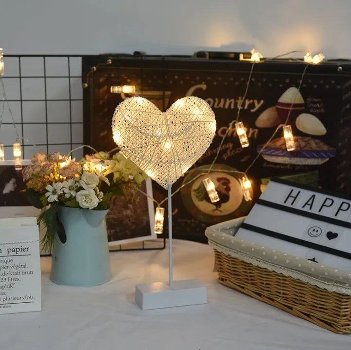 Rattan and copper wire LED table lamp in a star, heart, or moon shape on a wooden table.