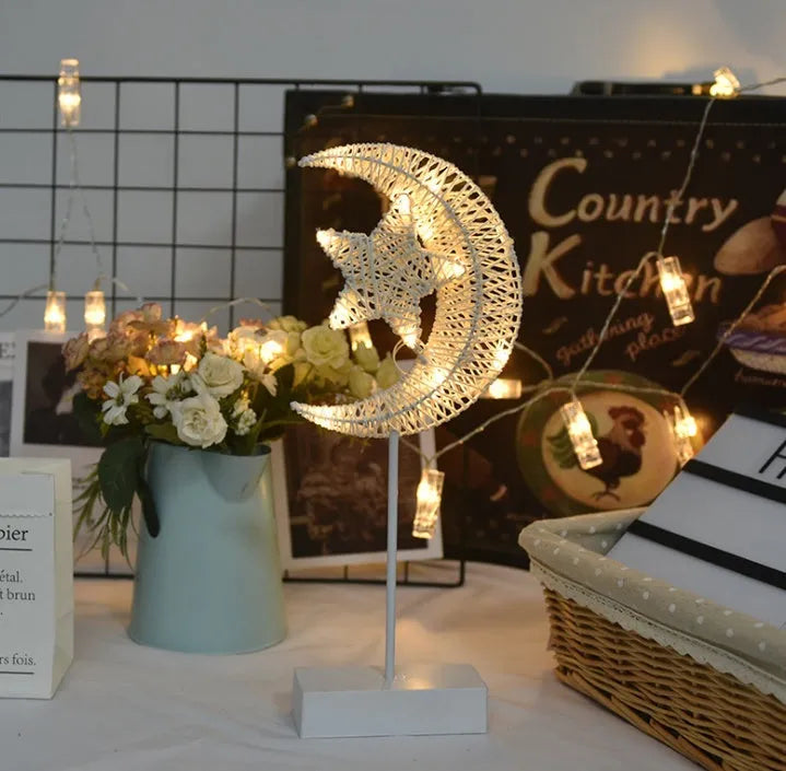 Rattan and copper wire LED table lamp in a star, heart, or moon shape on a wooden table.